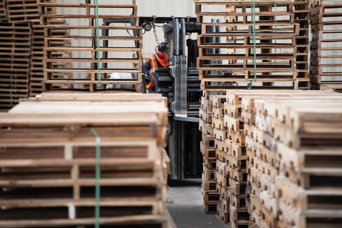 Recycled wooden pallets at a 48forty Solutions plant being moved by a forklift worker